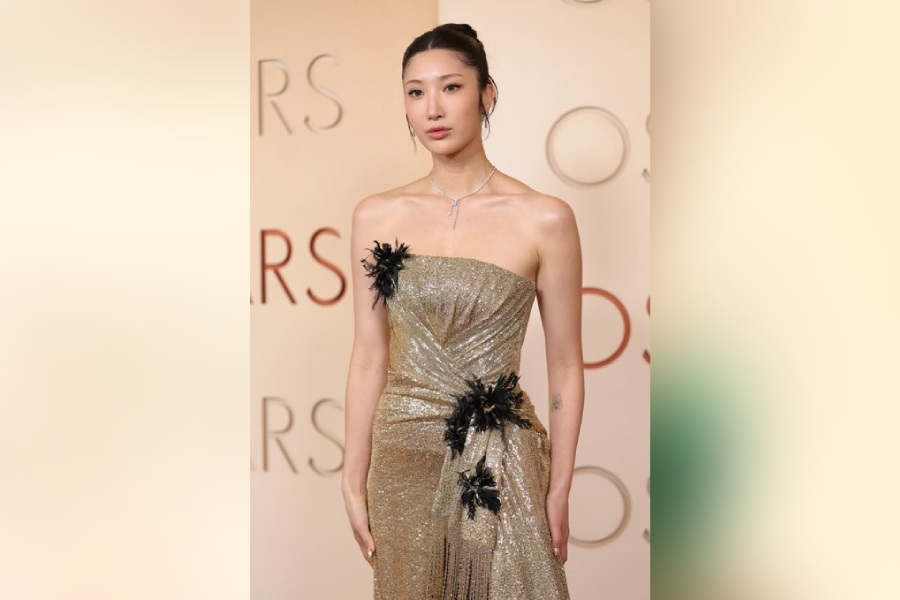 EJAE graced the Oscars 2026 red carpet in a gold sequined, strapless gown with black feather embellishments.